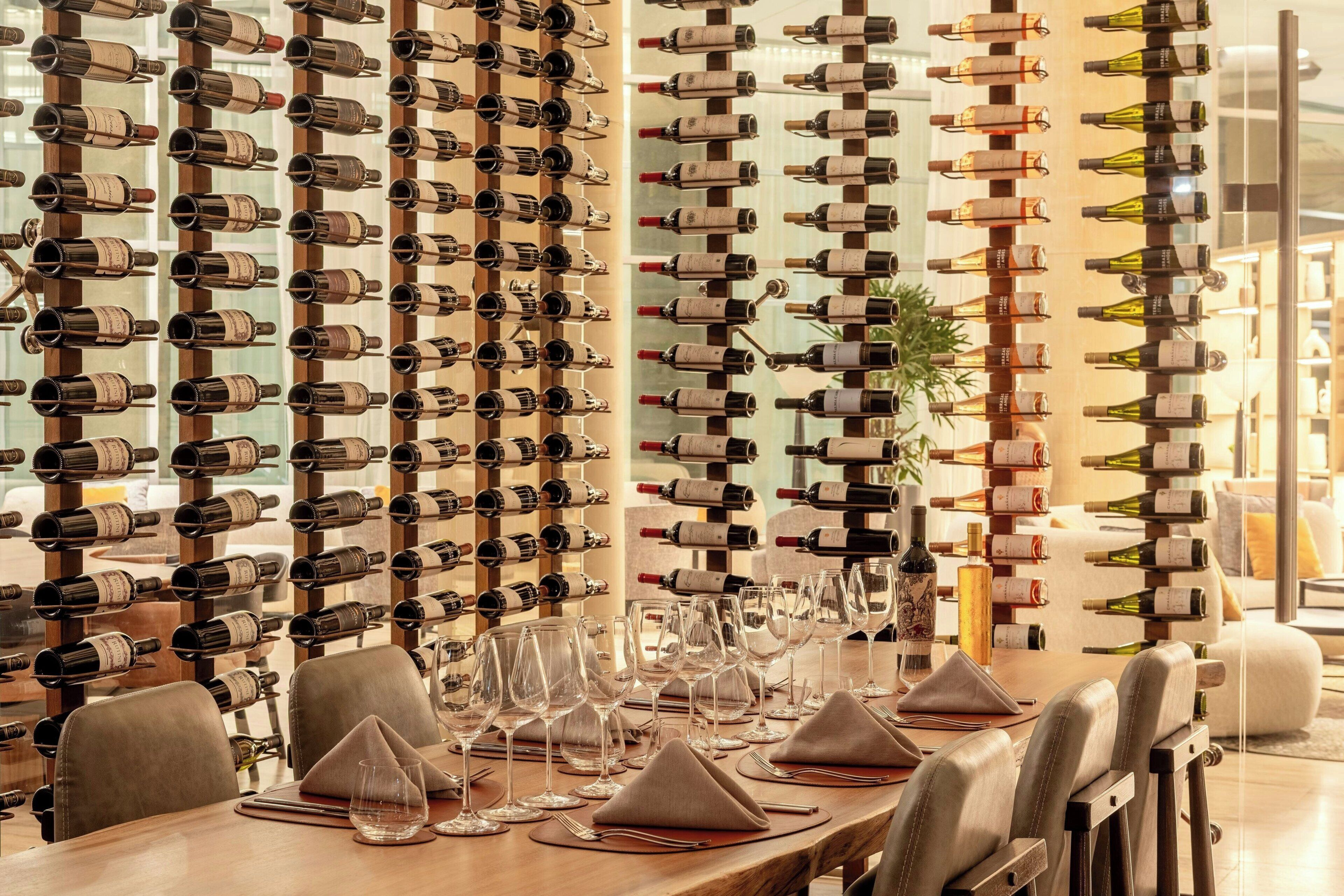 A restaurant interior with a long dining table set for a meal, surrounded by wine racks with bottles.