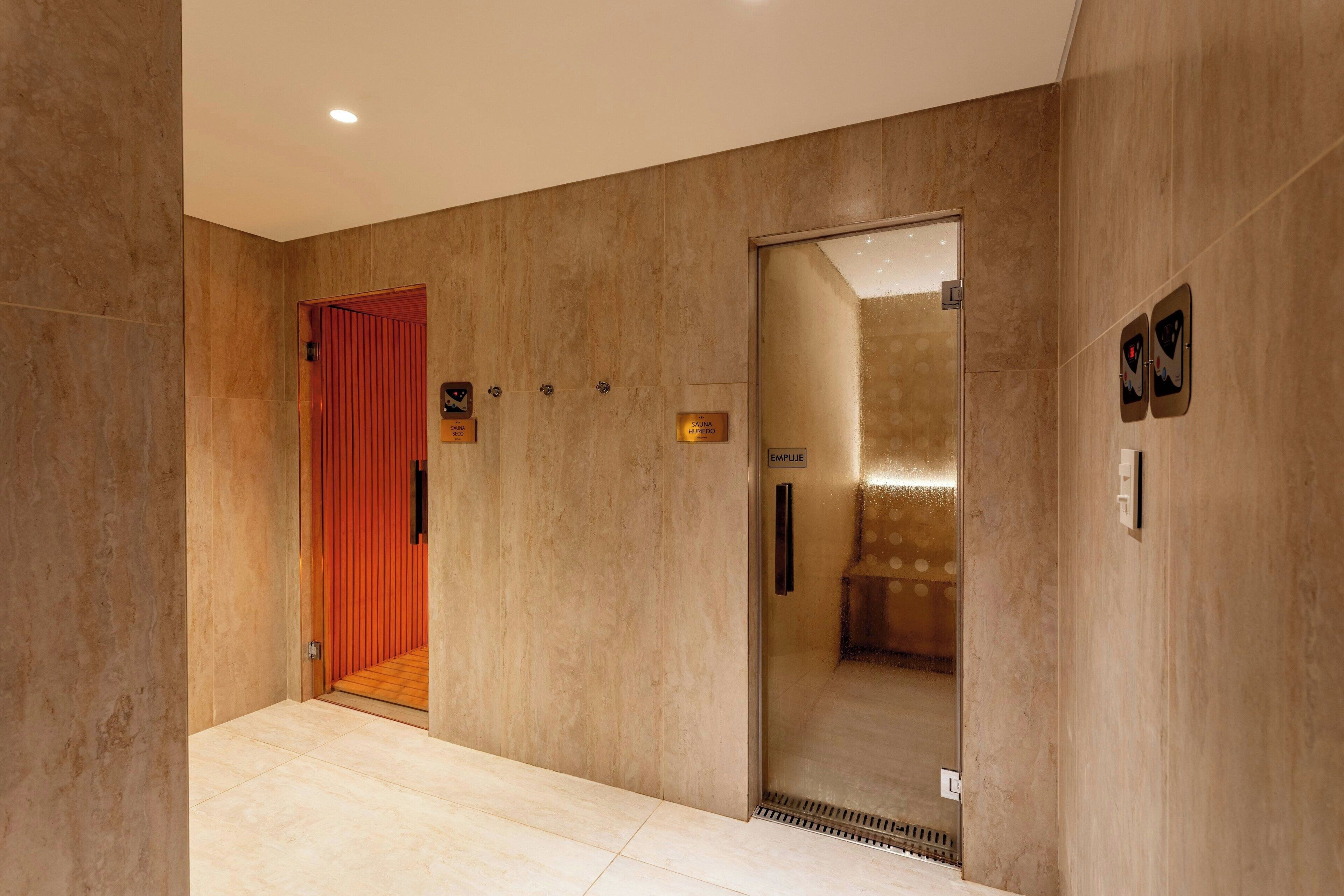 A modern elevator with a glass door, a red door, and a sign indicating 'SAUNA HUMEDO'.