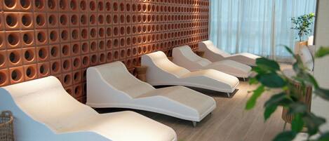 Un moderno spa con pared de madera con abertura circulares, tres sillas reclinables y un ventanal con cortinas translúcidas.
