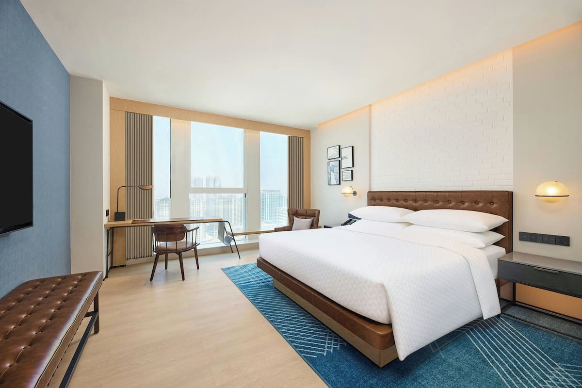 Moderni hotellihuone, jossa on suuri sänky, työpöytä ja näkymä kaupunkiin.