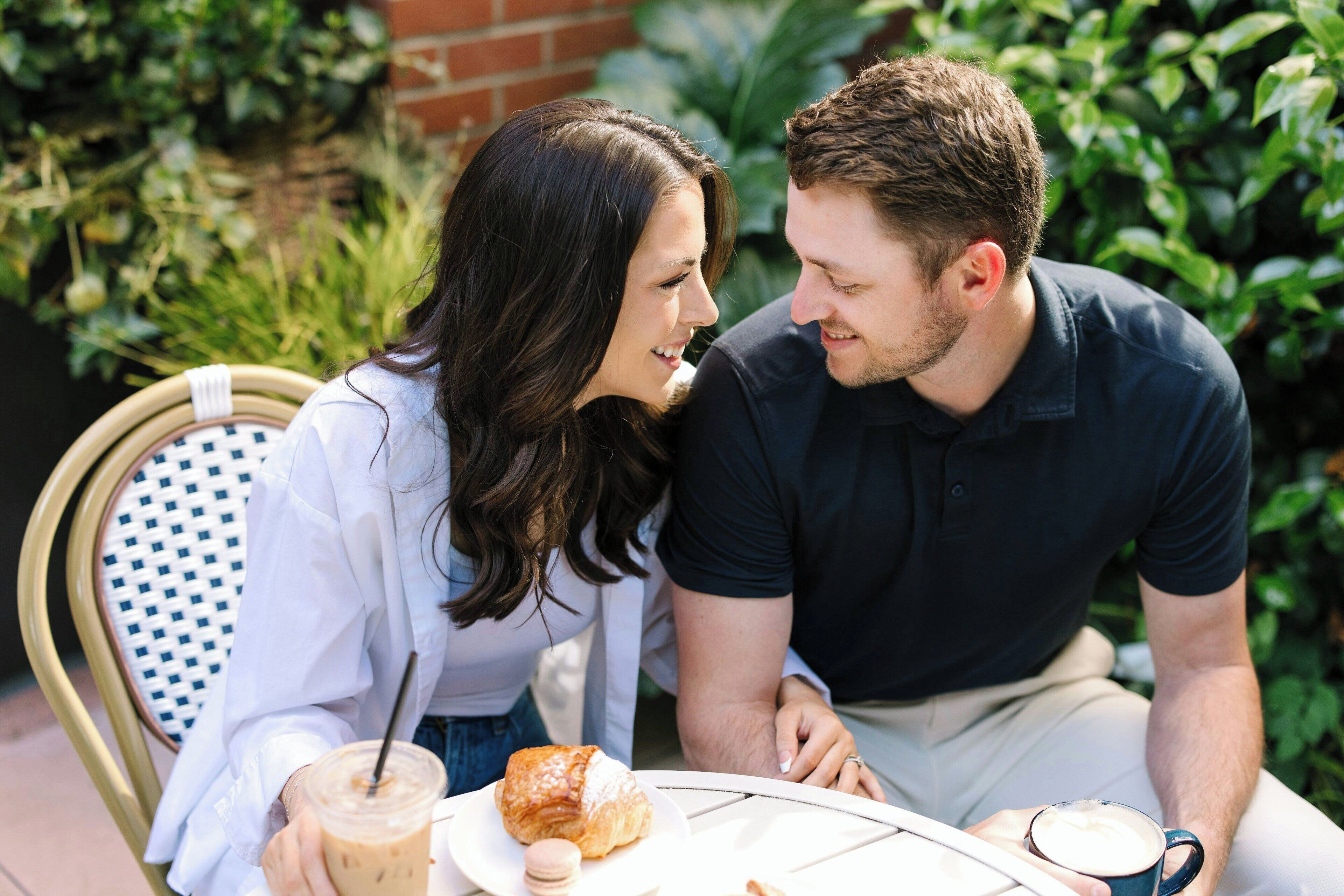 A couple sitting at an outdoor table with a drink and pastry.