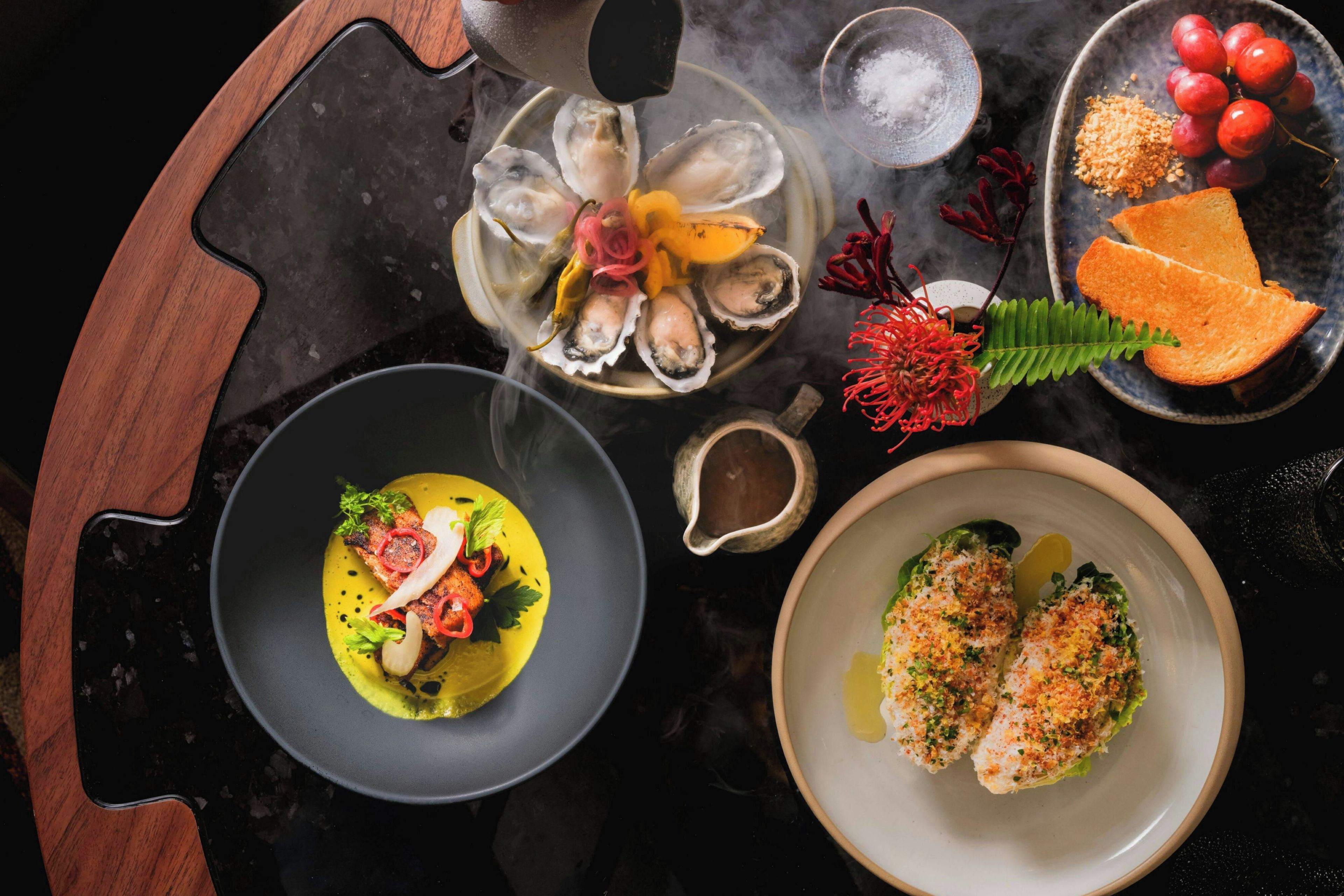 A variety of dishes including seafood, bread, and a dessert, arranged on a black table with a wooden edge.