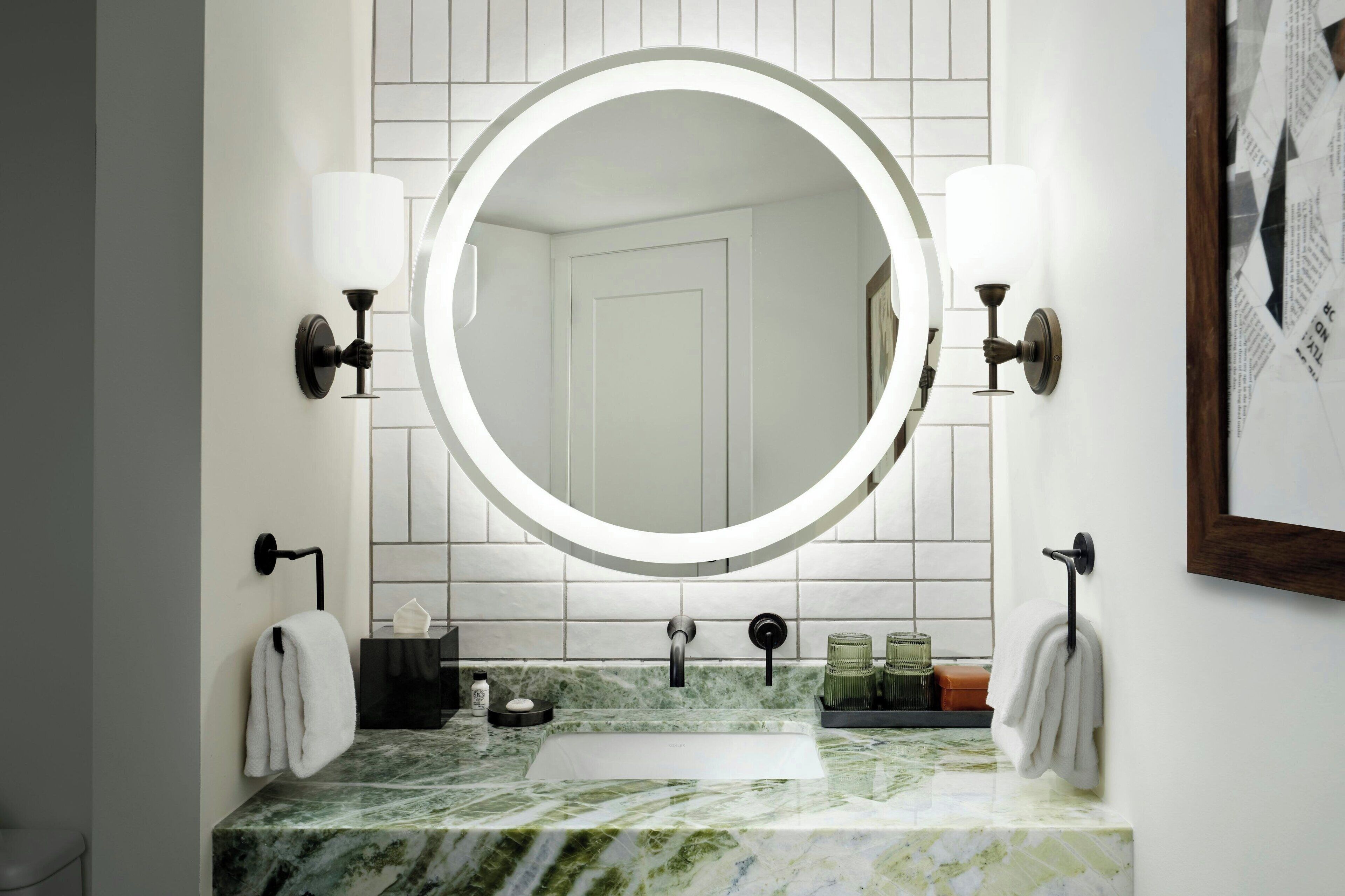 Een badkamer met een marmeren wastafel, een ronde spiegel met verlichting, en twee handdoekrekken.
