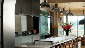 Une cuisine moderne dotée d’un îlot central, de tabourets de bar, de luminaires suspendus et offrant une vue à travers une arche.