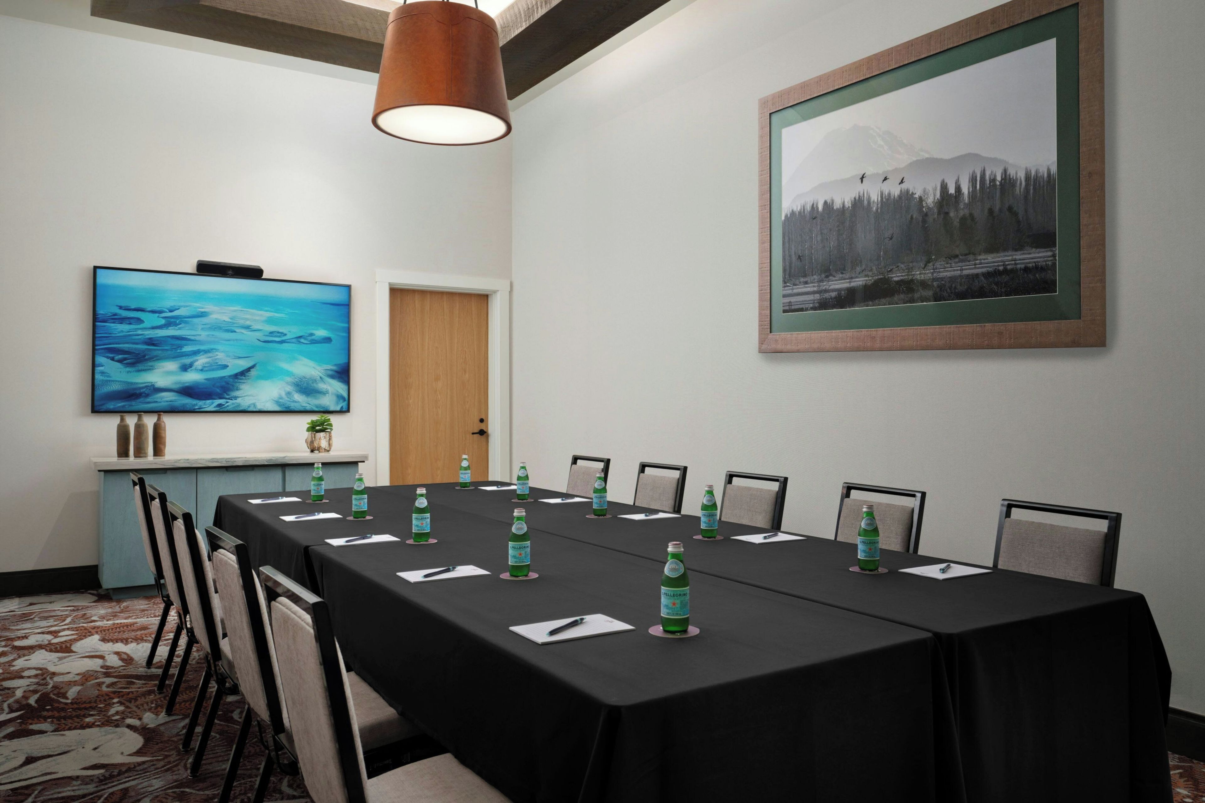 A conference room with a long table, chairs, a television, and a framed picture on the wall.