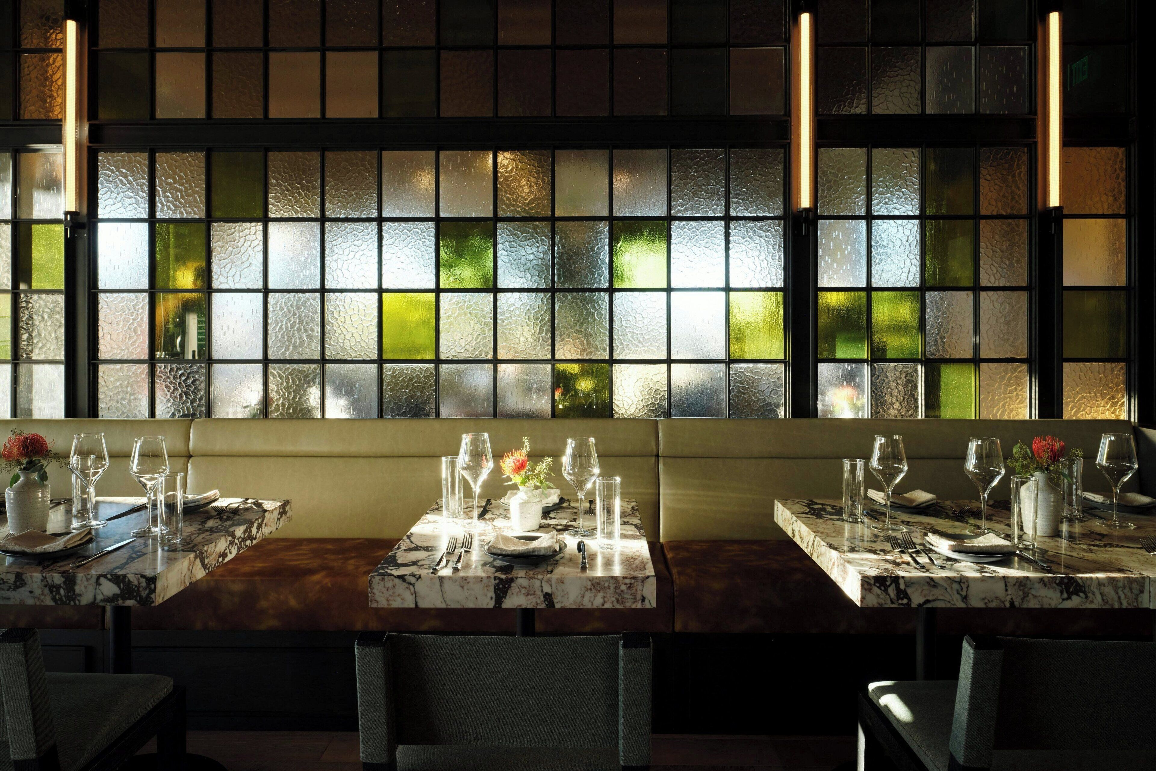 A restaurant with a marble table set for two, a cushioned bench, and a view through a textured glass partition.
