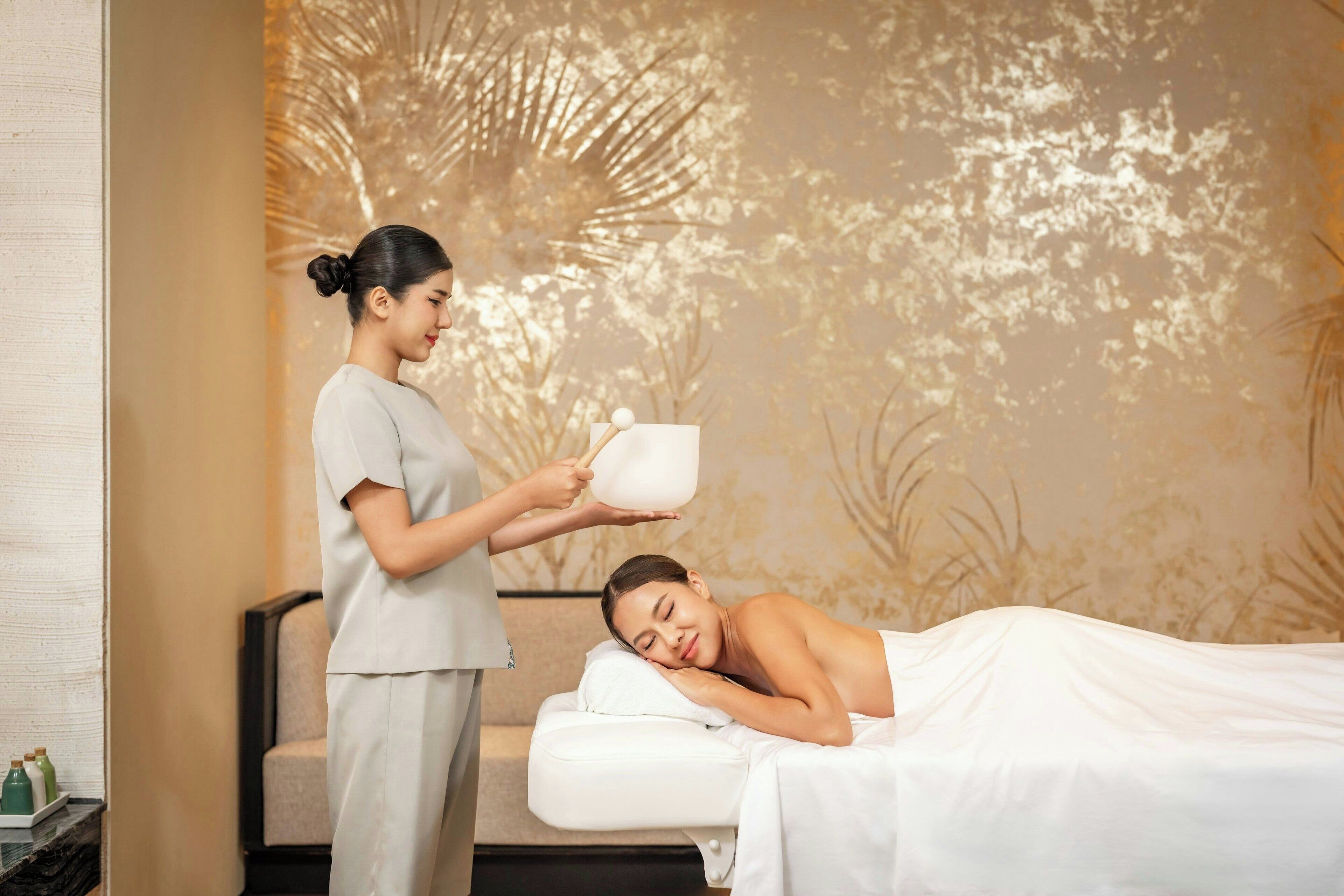 A spa room with a massage table, a massage therapist, and a wall with a nature-themed mural.