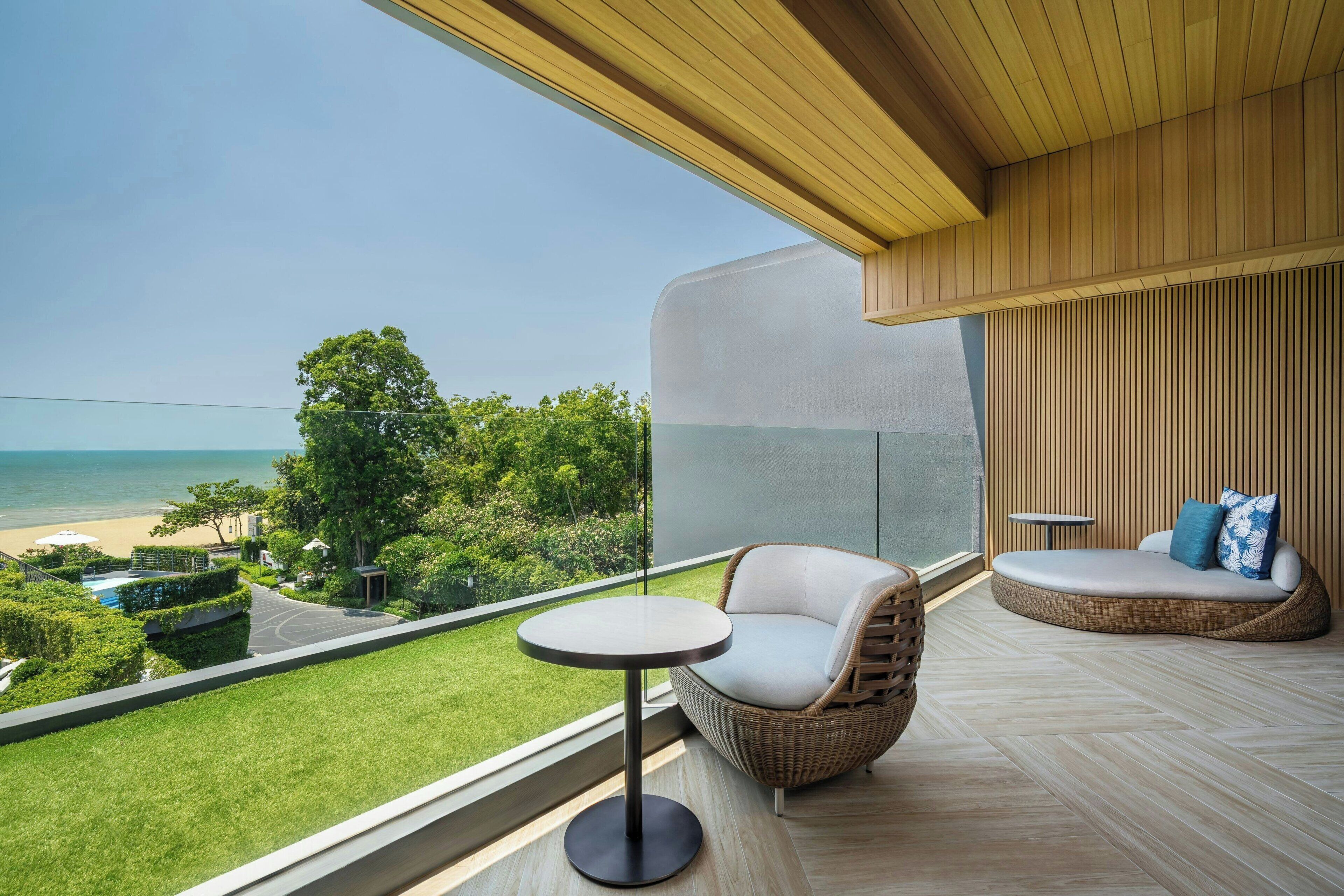 A balcony with a view of the beach, a wicker chair, a round table, and a cushioned seating area.