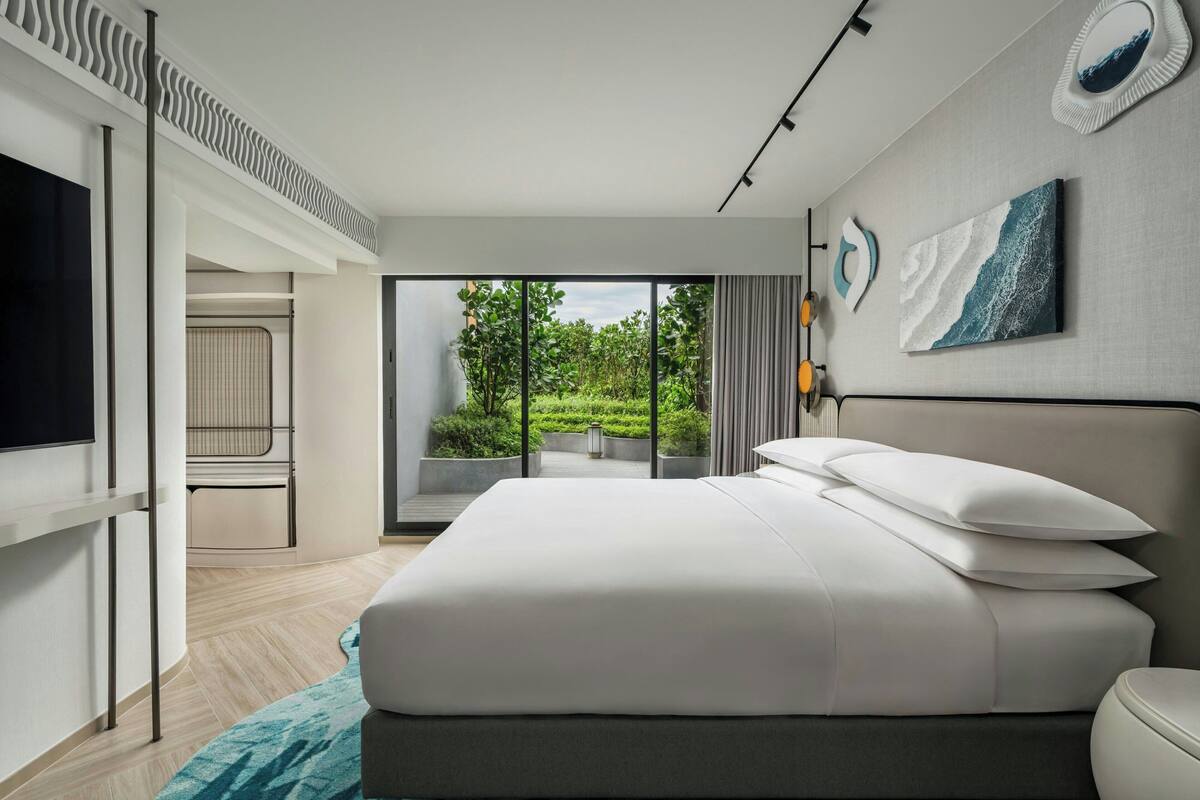 Ein modernes Schlafzimmer mit einem großen Bett, einem Fernseher und Blick ins Grüne durch die Glastür.