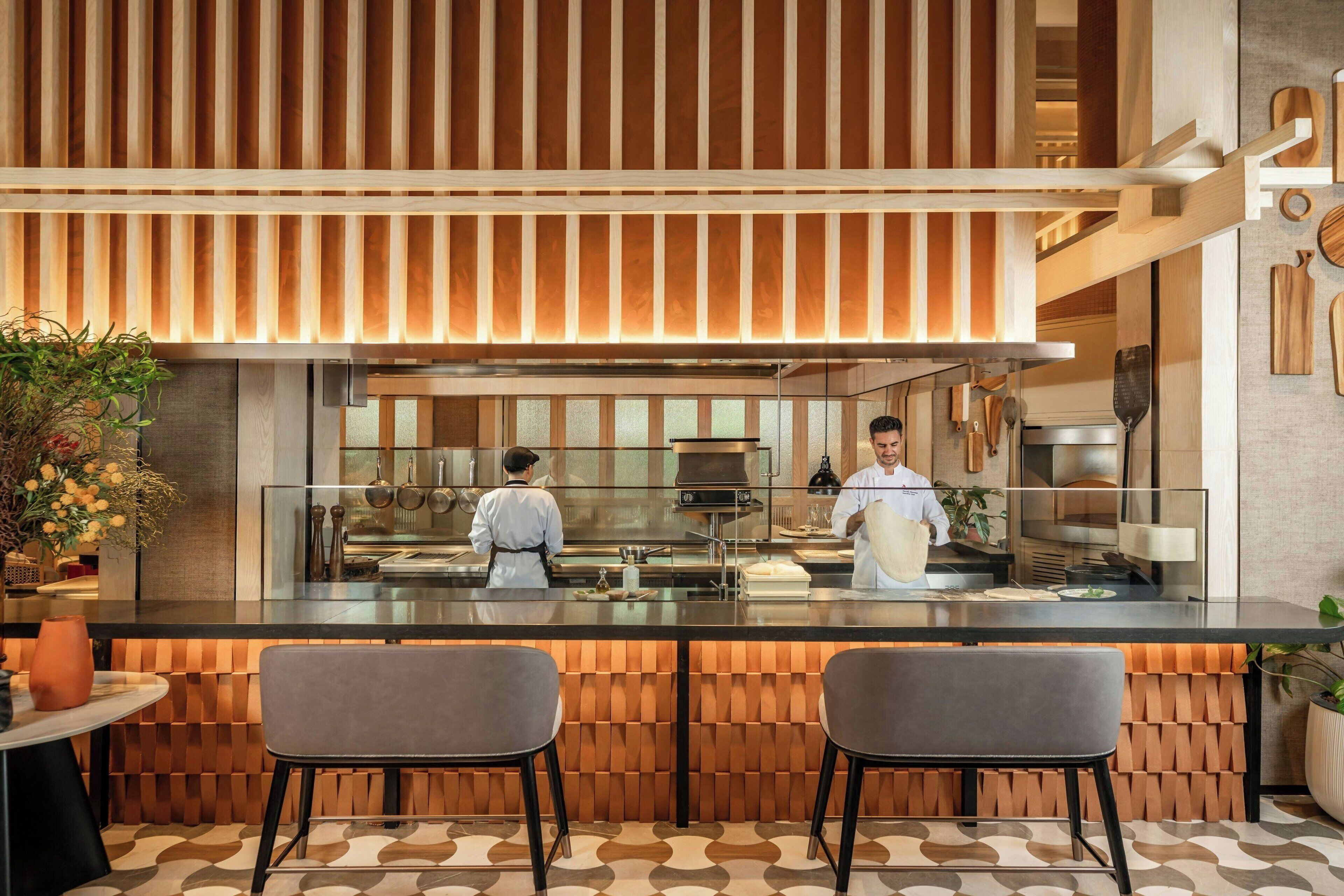 A modern kitchen with a chef preparing food, a bar area with two stools, and a patterned floor.