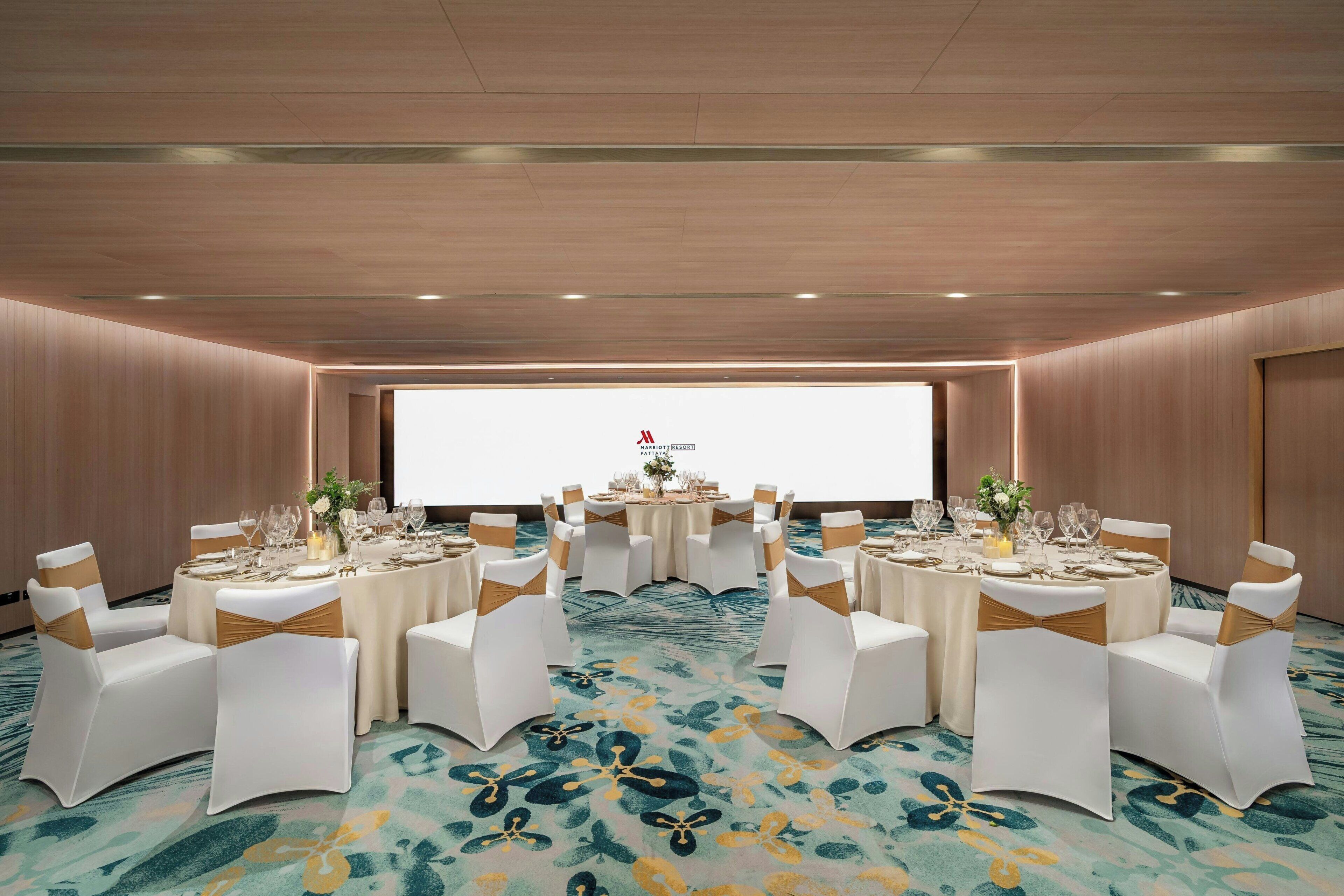 A conference room with round tables, white chairs with gold sashes, and a carpeted floor.