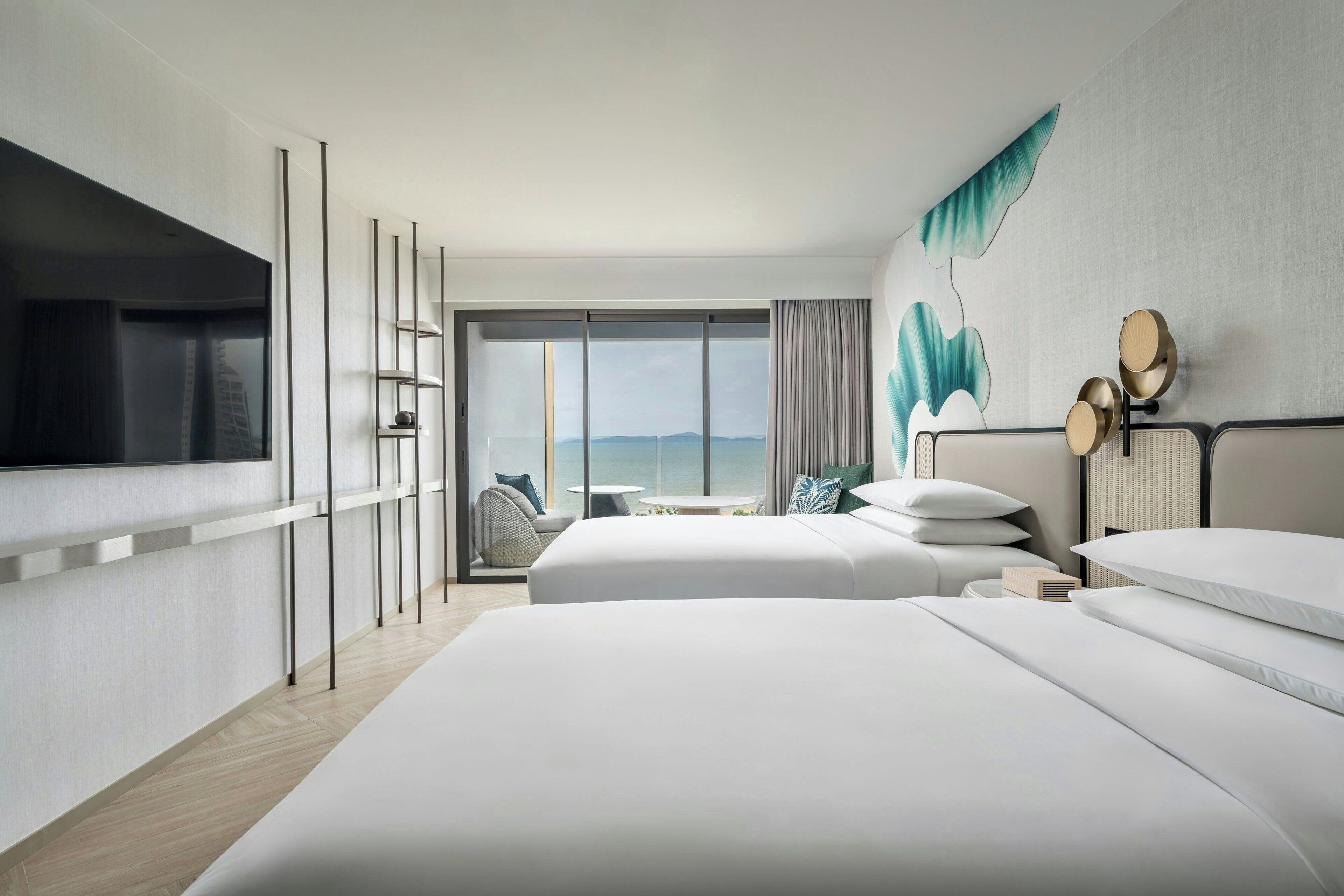 A modern hotel room with two beds, a large window with a view, a flat-screen TV, and a wall-mounted shelf.