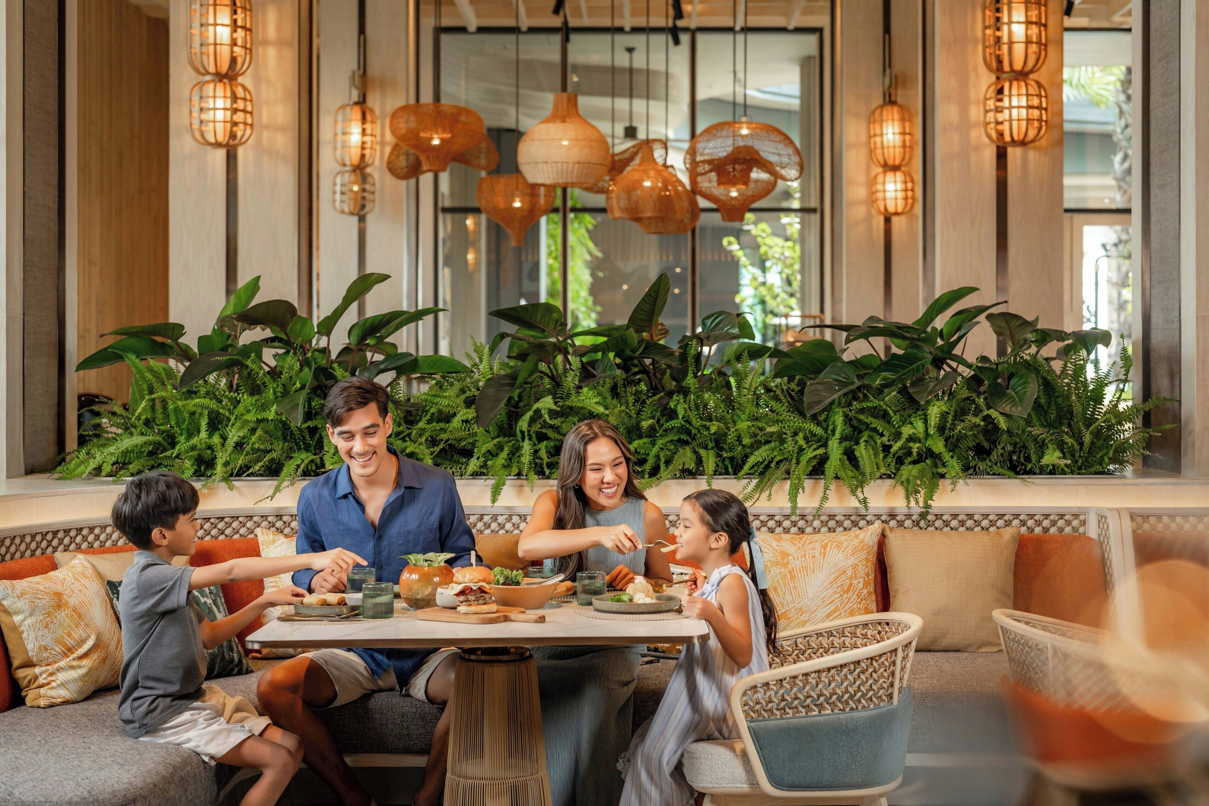 A family dining at a table with a view of indoor plants and hanging lights.