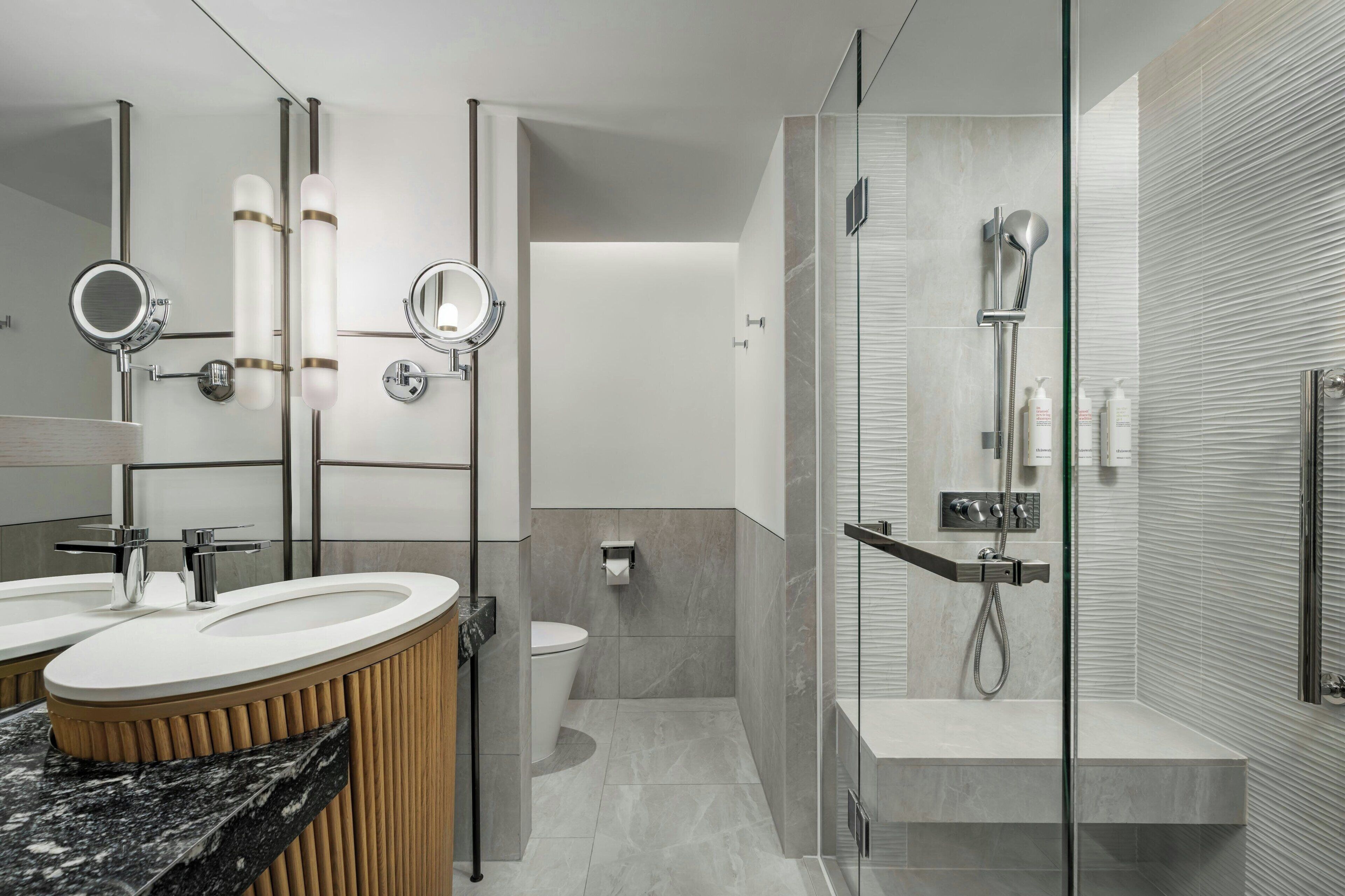 Un baño moderno con tocador, dos lavamanos, inodoro y zona de ducha con mampara de vidrio.