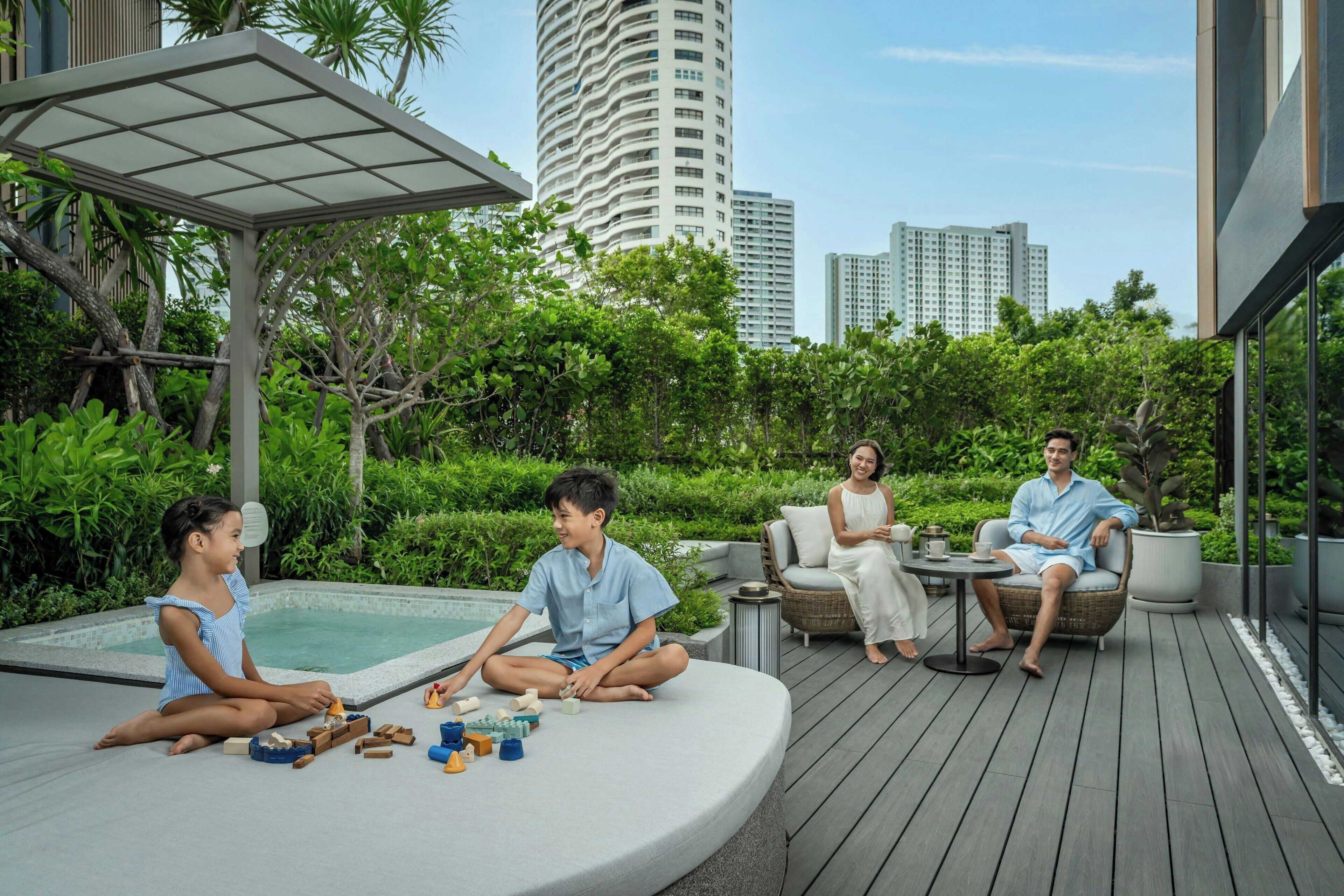 A rooftop deck with a pool, greenery, and modern buildings in the background.