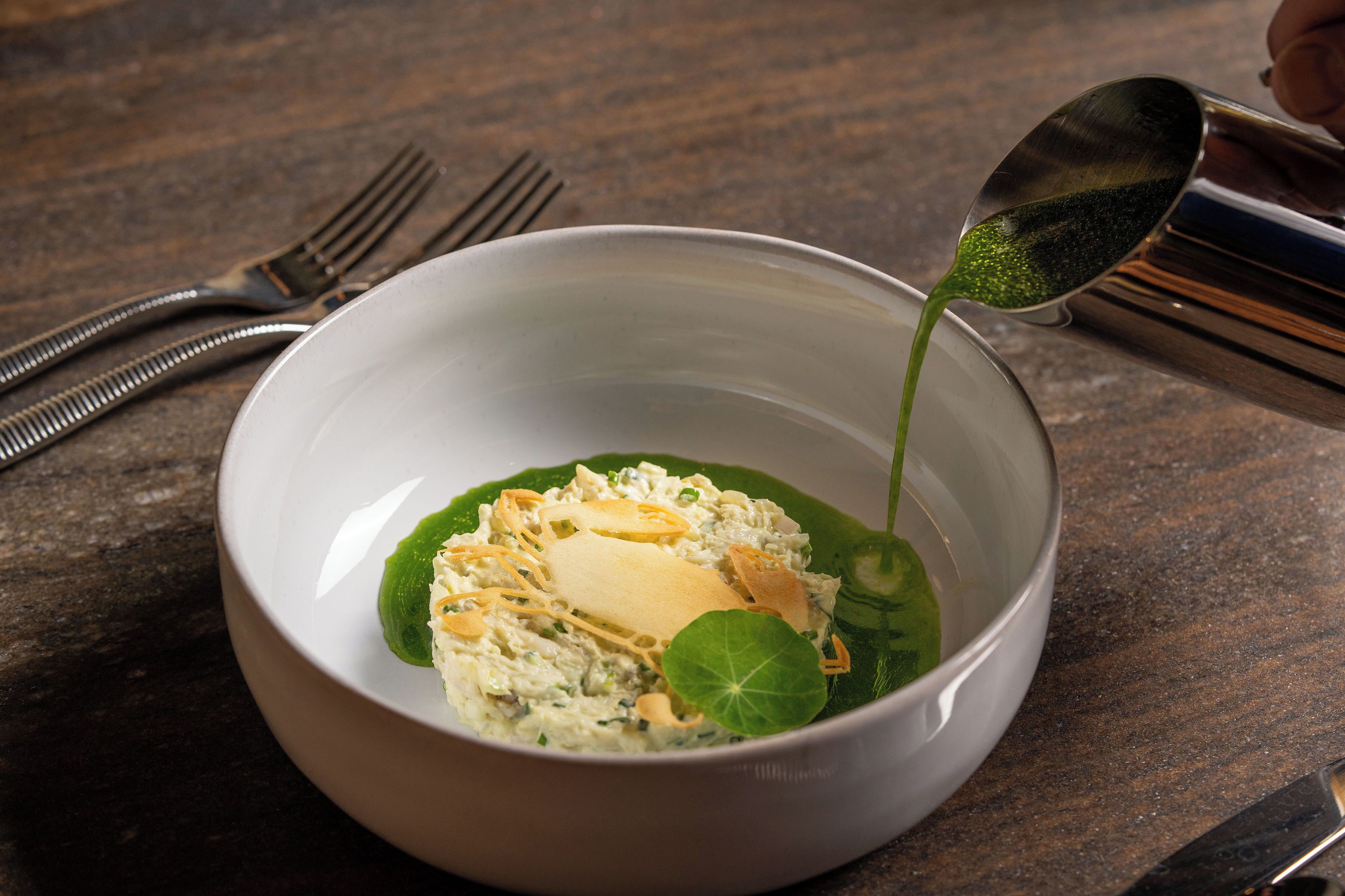 Eine Schüssel Suppe, aus der eine Kelle grüne Flüssigkeit schöpft.