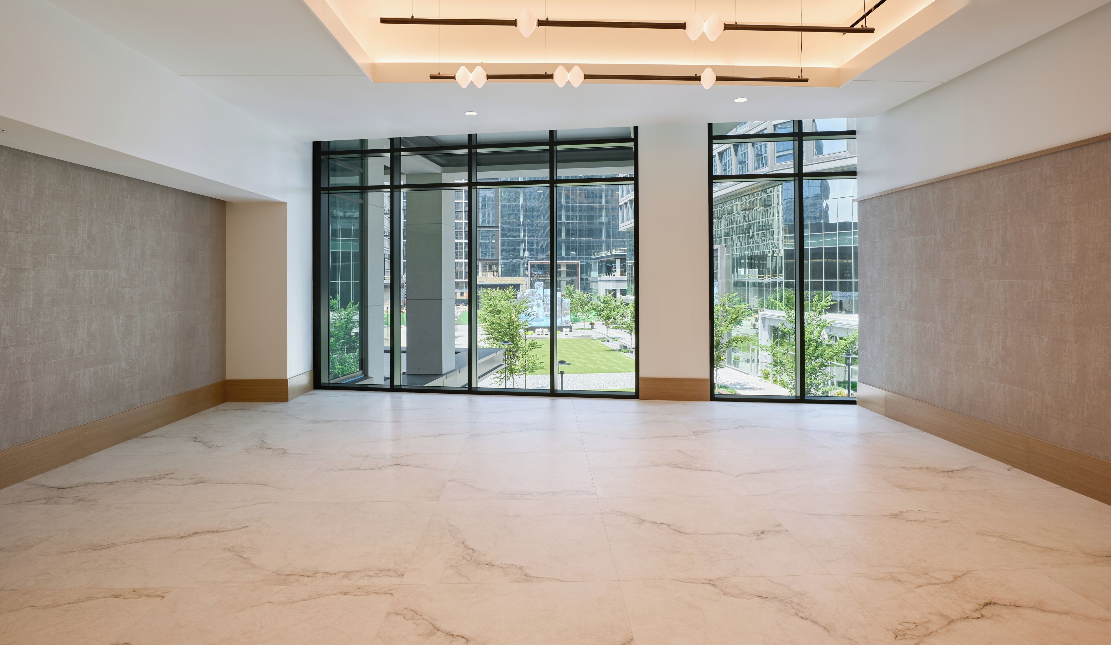 A spacious room with a large glass door leading to an outdoor area, featuring a marble floor and modern lighting fixtures.