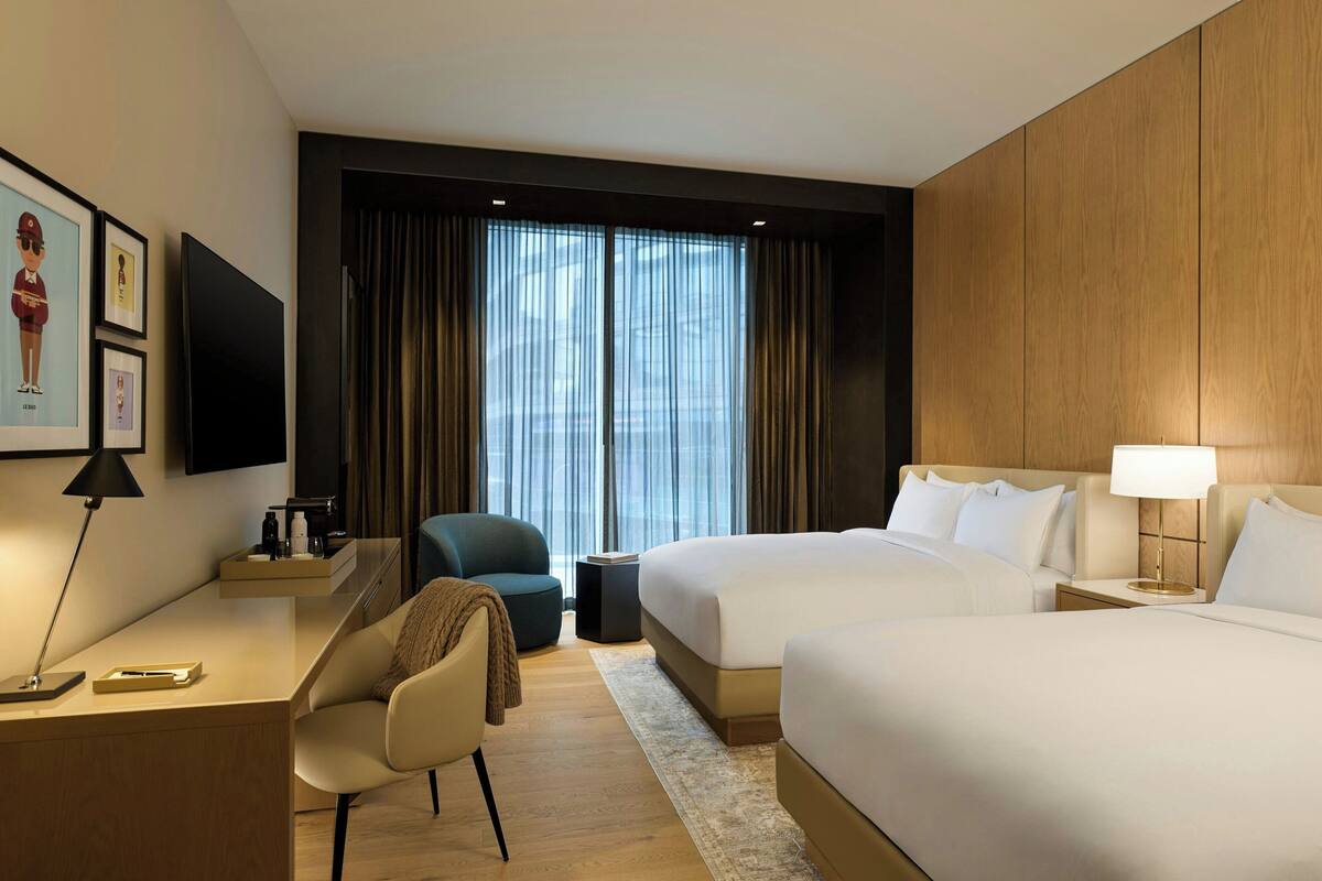 Habitación de hotel con una cama grande, un escritorio, una silla, un televisor y una ventana con cortinas.