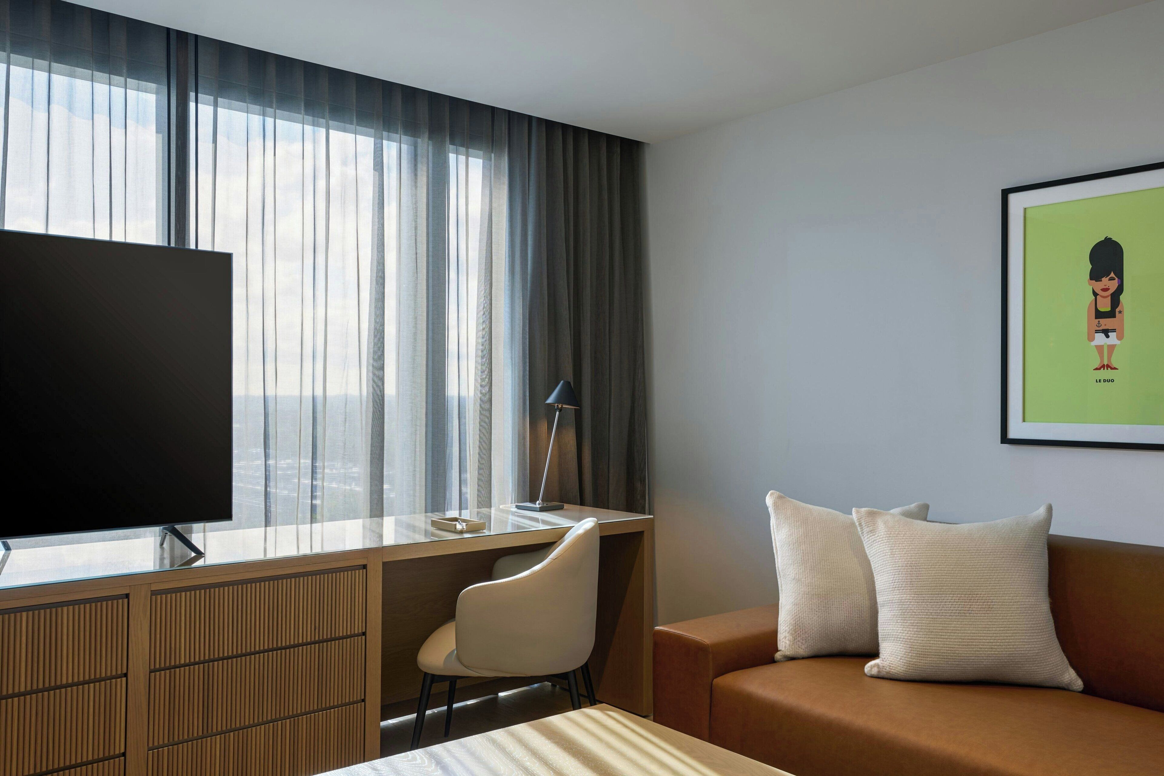 Ein Hotelzimmer mit einem großen Flachbildfernseher, einem Schreibtisch, einem Sessel, einer Couch und einem gerahmten Bild an der Wand.