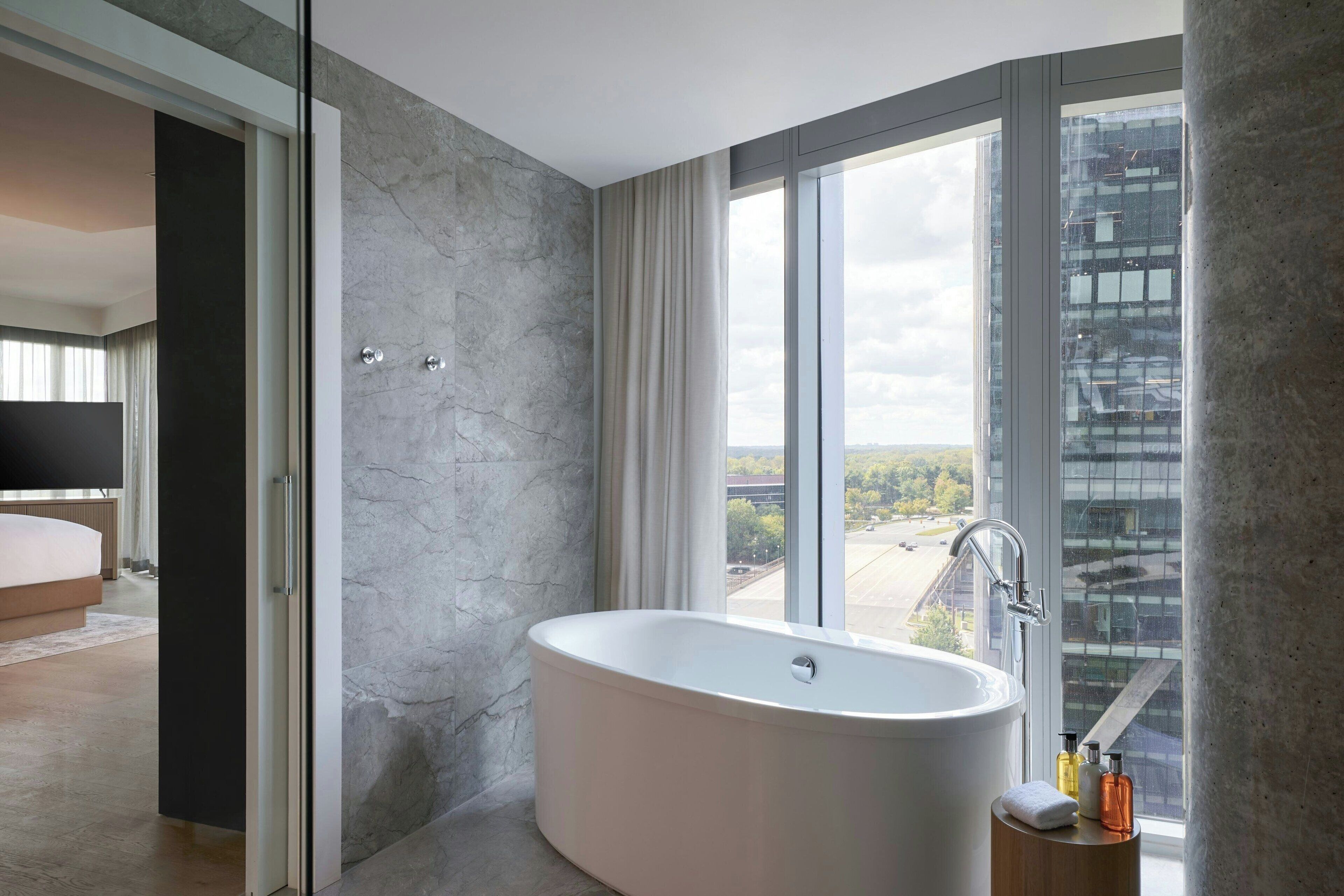 Un baño moderno con una bañera independiente, un amplio ventanal con vistas a la ciudad y un diseño minimalista.