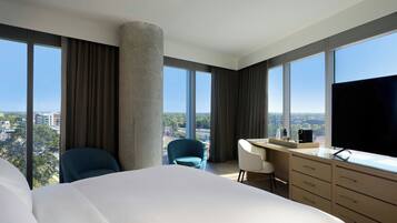 A hotel room with a large bed, a desk, a chair, a TV, and a view of the city.