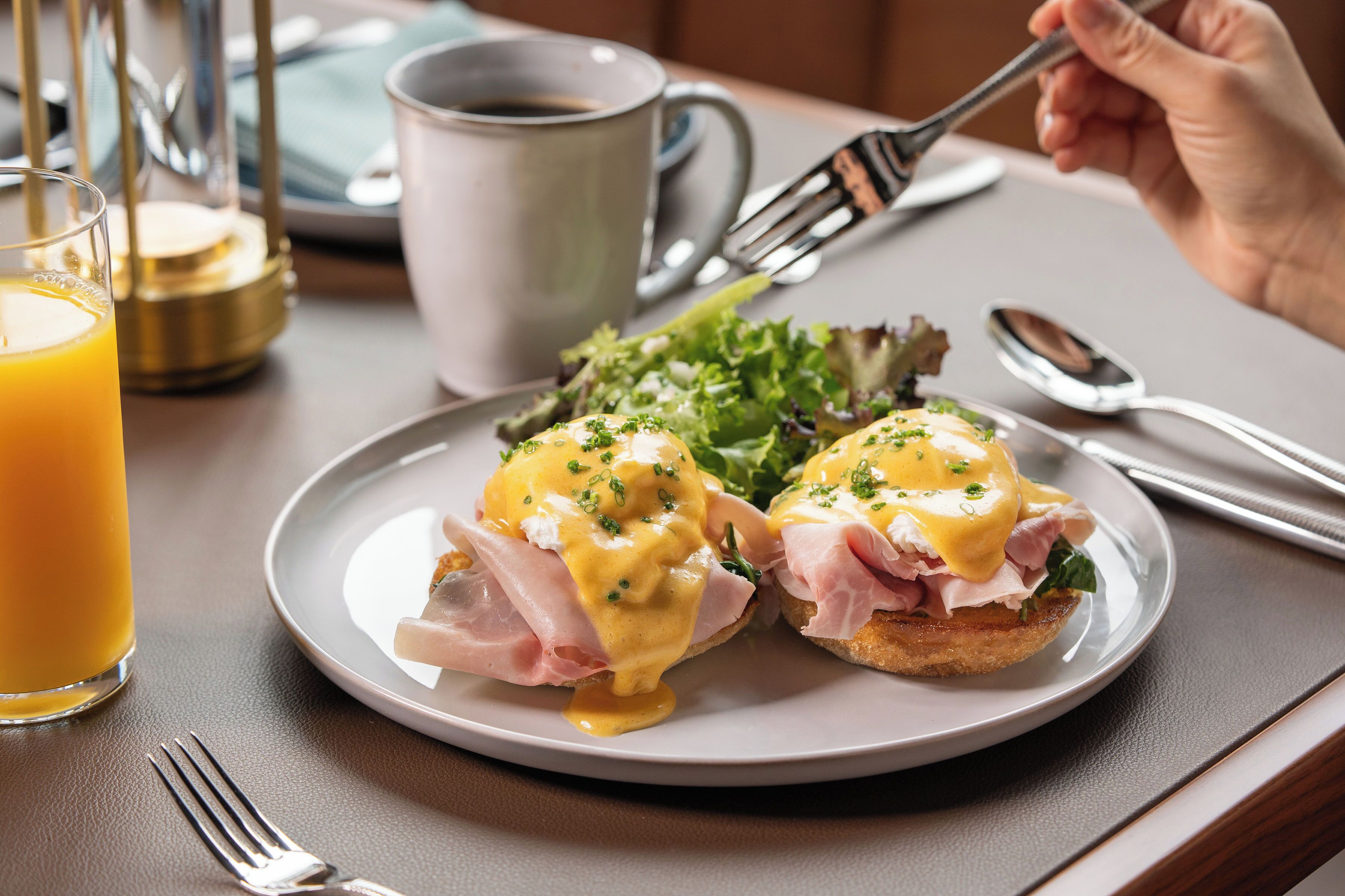 A breakfast plate with eggs benedict, a glass of orange juice, and a cup of coffee on a table.