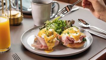 A breakfast plate with eggs benedict, a glass of orange juice, and a cup of coffee on a table.