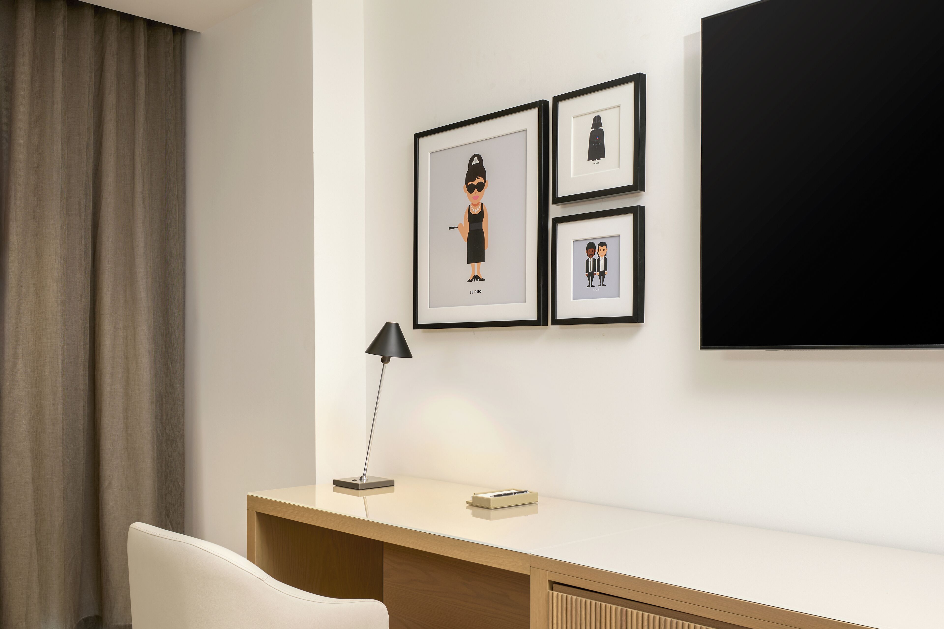 Ein Hotelzimmer mit Schreibtisch, Stuhl, Lampe und drei gerahmten Bildern an der Wand.