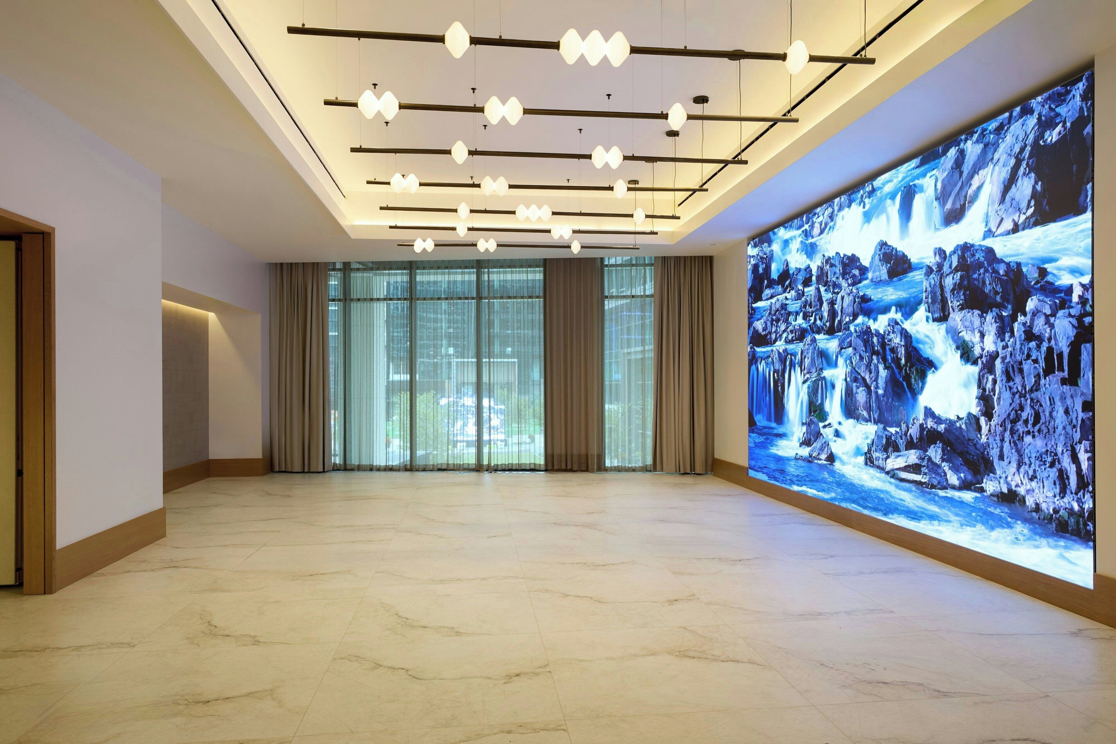 A spacious lobby with a large digital waterfall display, a modern ceiling design with hanging lights, and a marble floor.