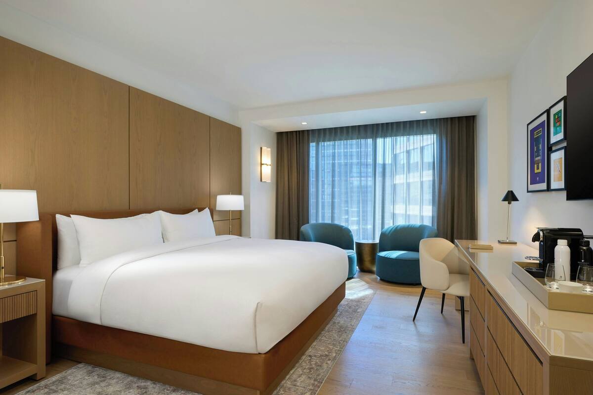 Habitación de hotel con una cama grande, un escritorio con cafetera, una silla y vistas a la ciudad desde la ventana.