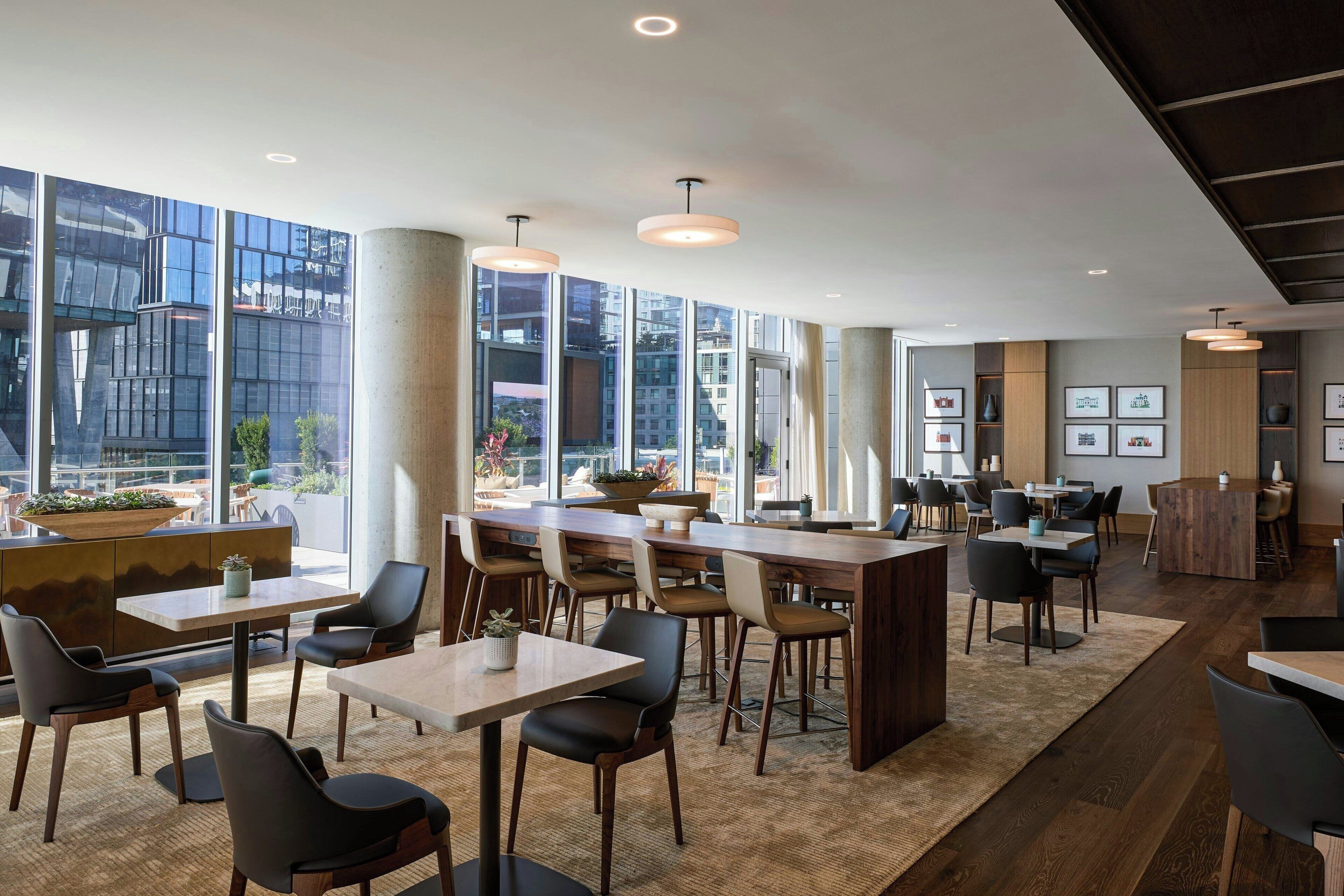 Un restaurante moderno con techos altos, amplios ventanales y una combinación de mobiliario de madera y tapizado.