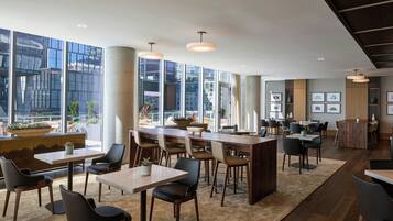 Un restaurante moderno con techos altos, amplios ventanales y una combinación de mobiliario de madera y tapizado.