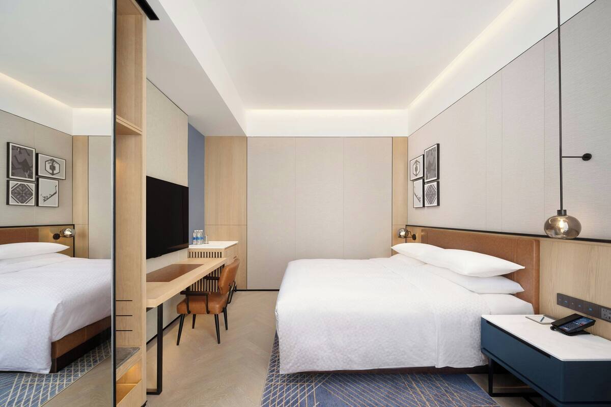 Een hotelkamer met twee bedden, een bureau, een stoel, een televisie en een nachtkastje met een lamp.