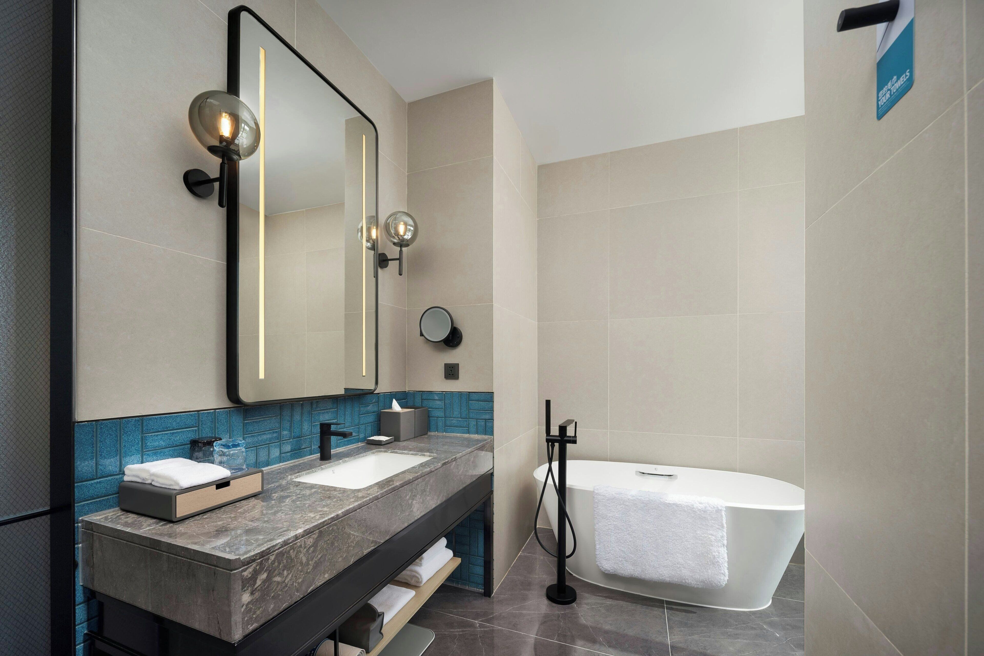 Une salle de bain moderne avec un grand miroir, deux lavabos, une baignoire et un porte-serviettes.