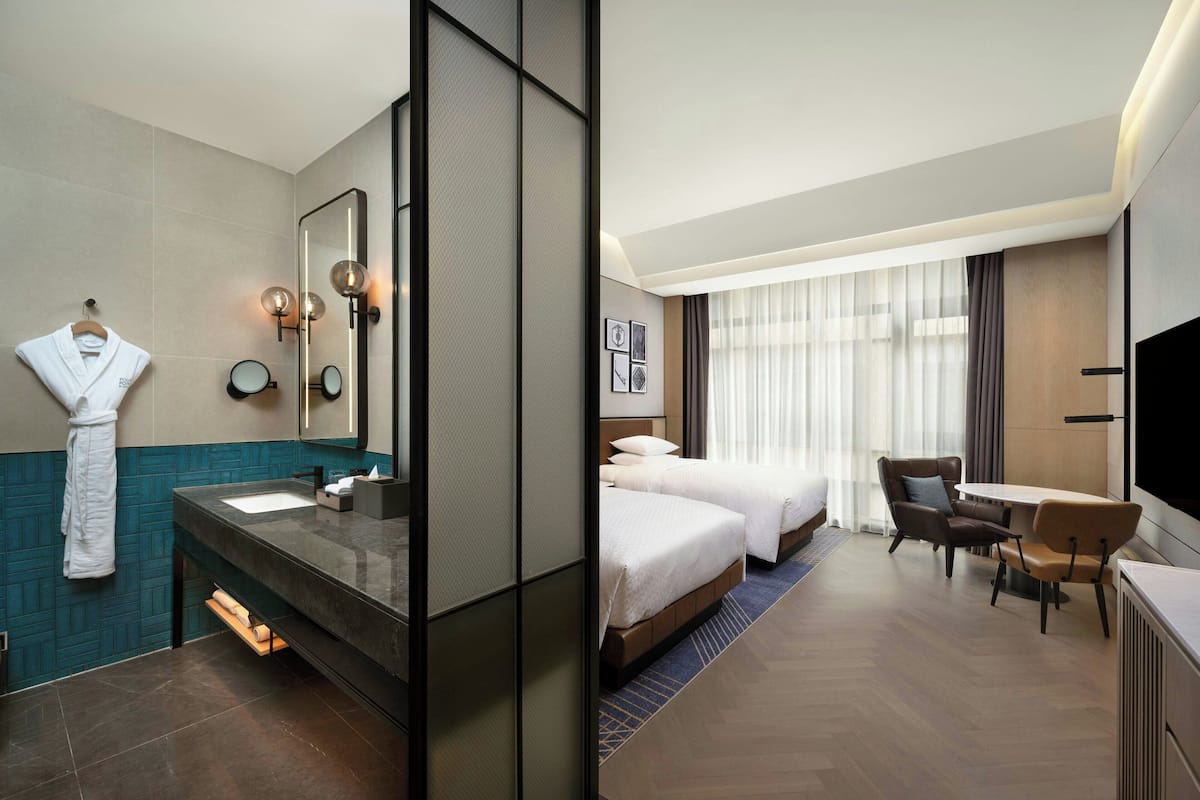 Een hotelkamer met een badkamer, uitgerust met een grote spiegel, een wastafel en een handdoekhouder. De kamer beschikt over twee bedden, een bureau met stoel en een televisie.
