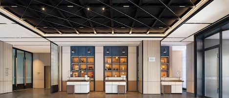 A modern hotel lobby with a geometric ceiling design, a reception desk, and a display of framed artwork.