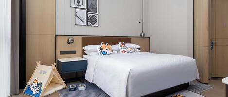 A modern hotel room with a neatly made bed, a small bedside table, a nightstand, a pet bed, and a pet bowl.
