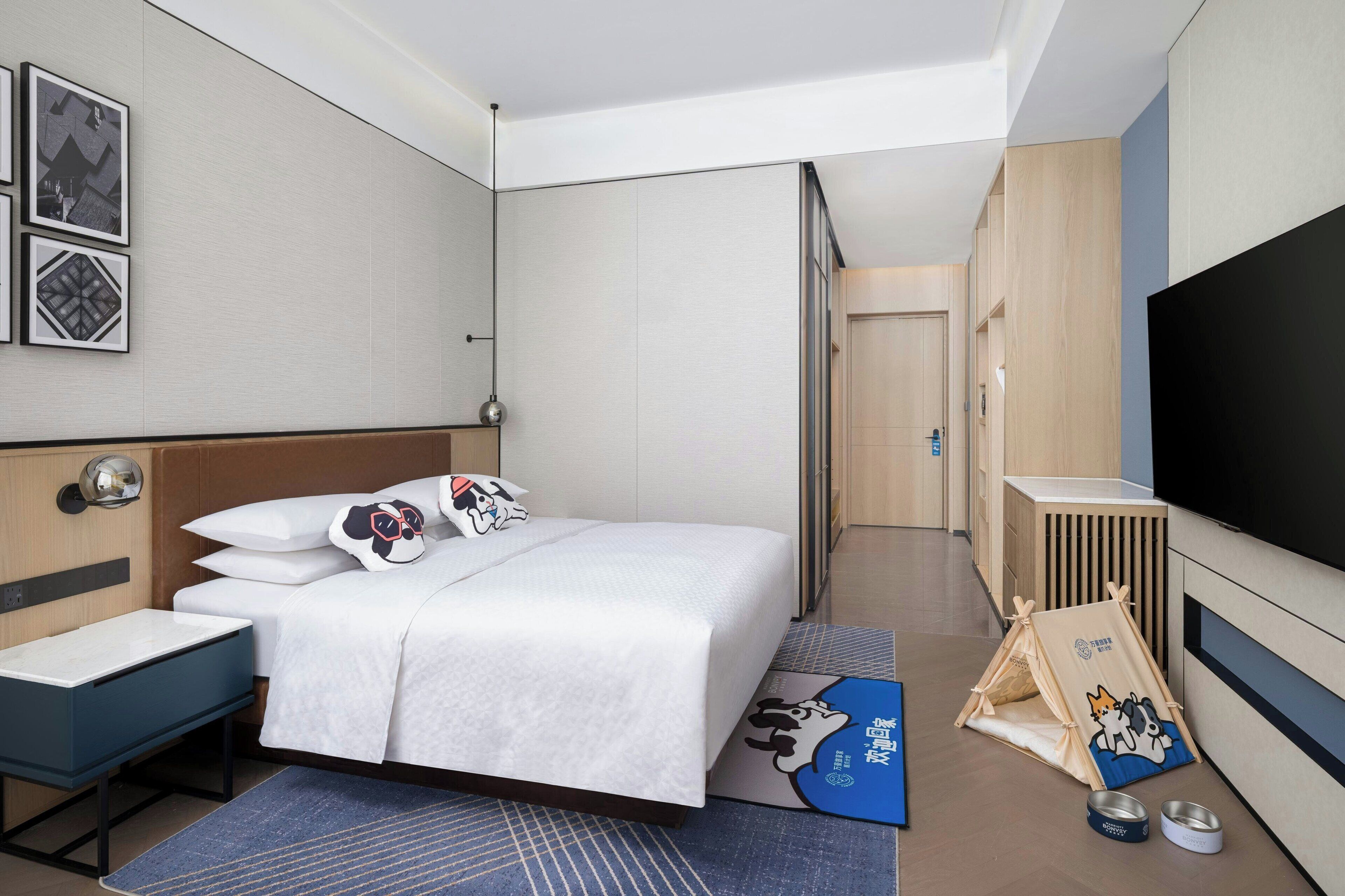 A hotel room with a bed, a desk, a TV, and a children's play area.