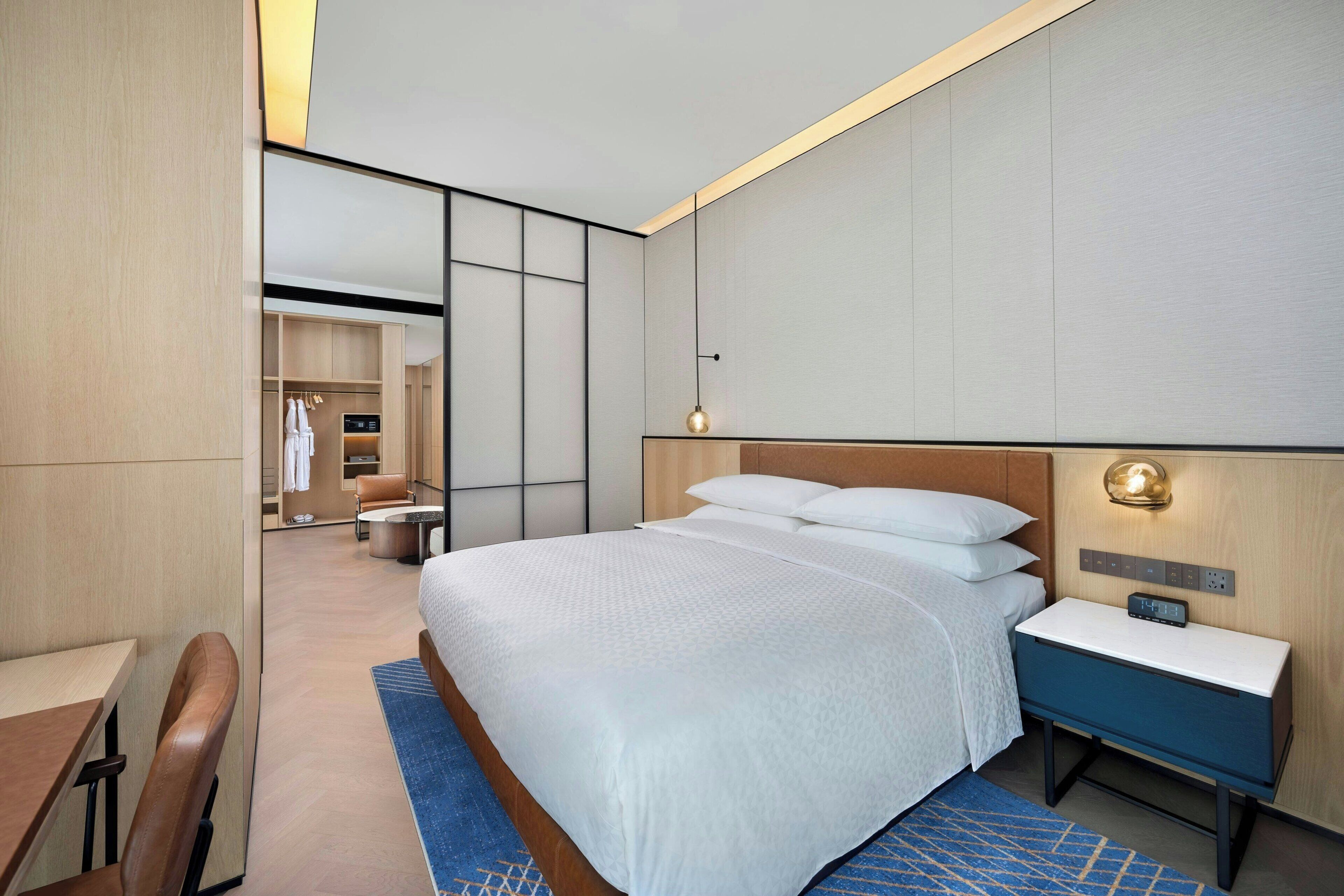 Una habitación de hotel moderna con una cama grande, mesita de noche y un espacio de escritorio.