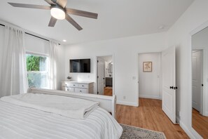 Un dormitorio con cama, ventilador de techo, televisor y vistas a la cocina.
