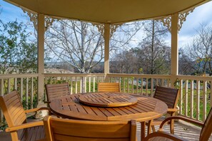 Un patio techado al aire libre con una mesa y sillas de madera redonda, rodeado por una barandilla blanca con pilares decorativos.