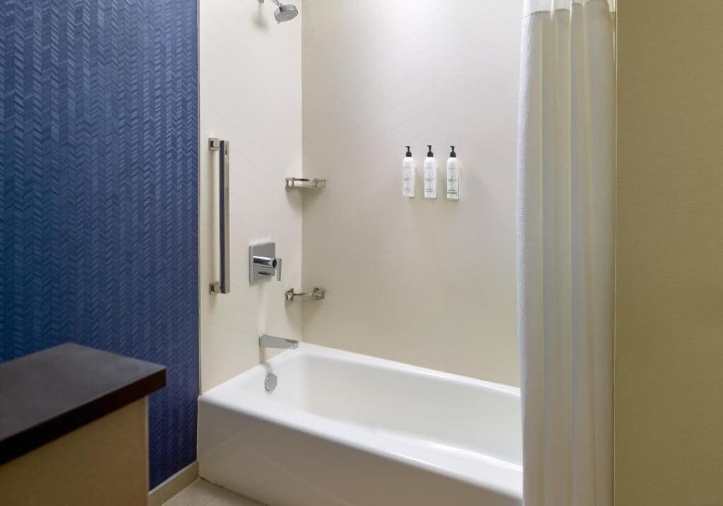 A bathroom with a white bathtub, a shower, and a blue textured wall. There are three bottles of toiletries on the wall.