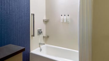 A bathroom with a white bathtub, a shower, and a blue textured wall. There are three bottles of toiletries on the wall.