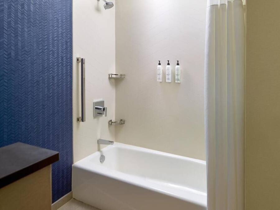 A bathroom with a white bathtub, a shower, and a blue textured wall. There are three bottles of toiletries on the wall.