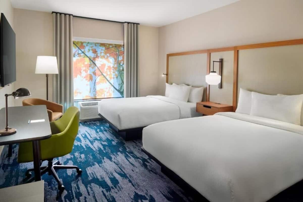 A hotel room with two beds, a desk with a chair, a TV, and a window with curtains.