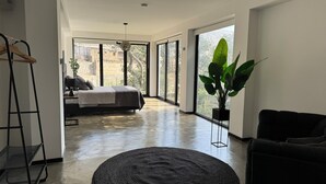 Una habitación amplia con una cama, un ventanal grande, una planta y un sofá negro.