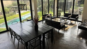 Amplia sala de estar con mesa de comedor, sofás y ventanas grandes que dan a una piscina y jardín.