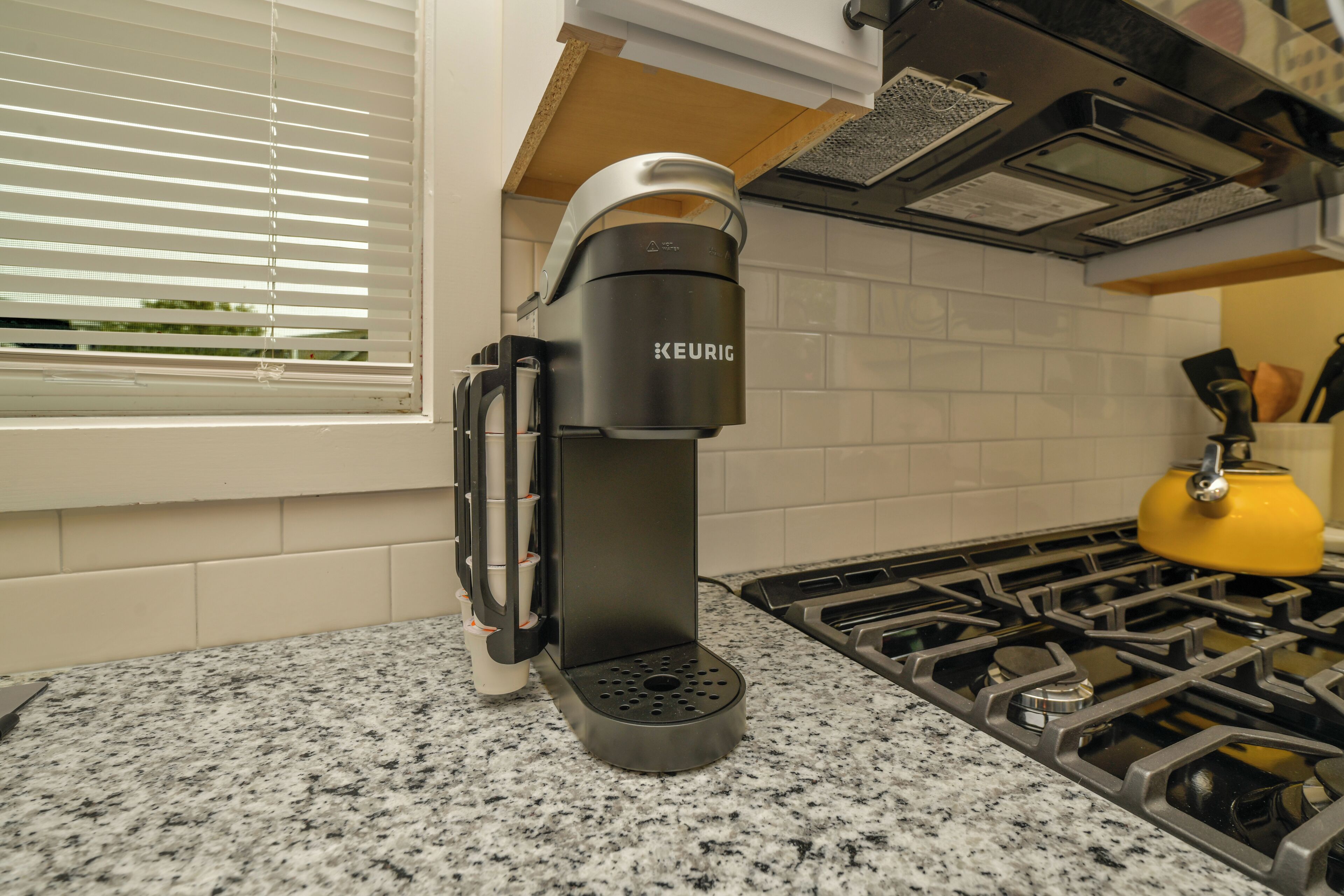 A modern kitchen with a Keurig coffee maker, a yellow kettle, and a gas stove.