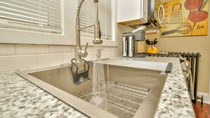 A kitchen with a stainless steel sink, a window with blinds, and a kitchen island with a yellow vase. - NEW! Upscale Private 3 Bed, Free Parking, W&D, Near MBTA, Backyard (Boston)