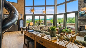 Un vaste espace de vie avec une grande fenêtre donnant sur un paysage pittoresque, une table à manger en bois et un décor moderne.